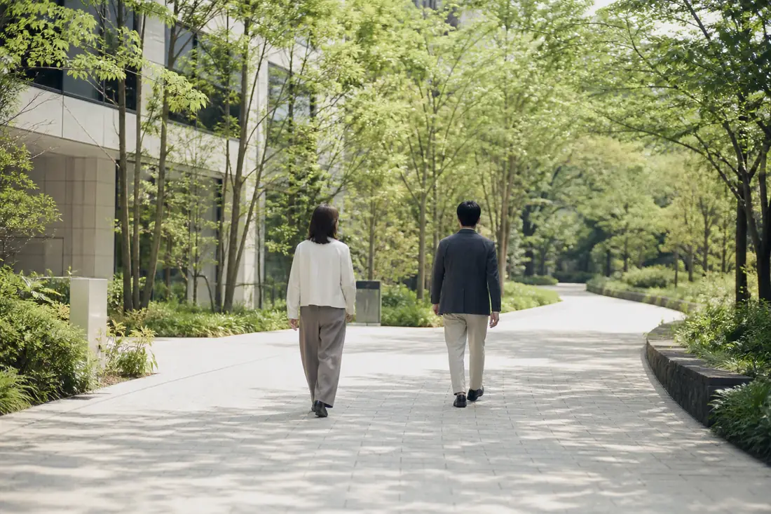 緑のある開放的な道を、ともに歩く二人の後ろ姿のイメージ